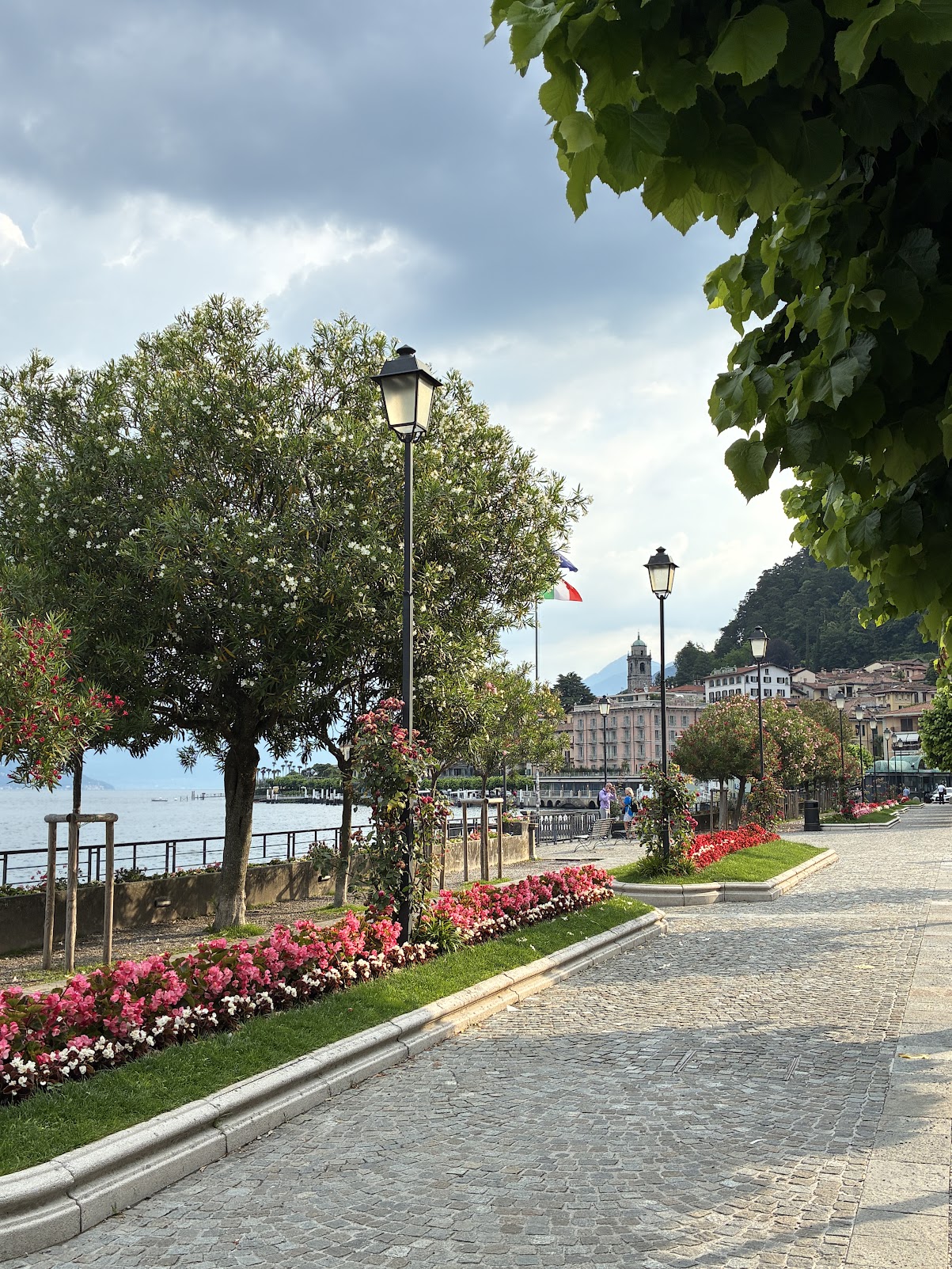 A lakeside promenade in Bellagio, paved and lined with flowerbeds, early in the morning